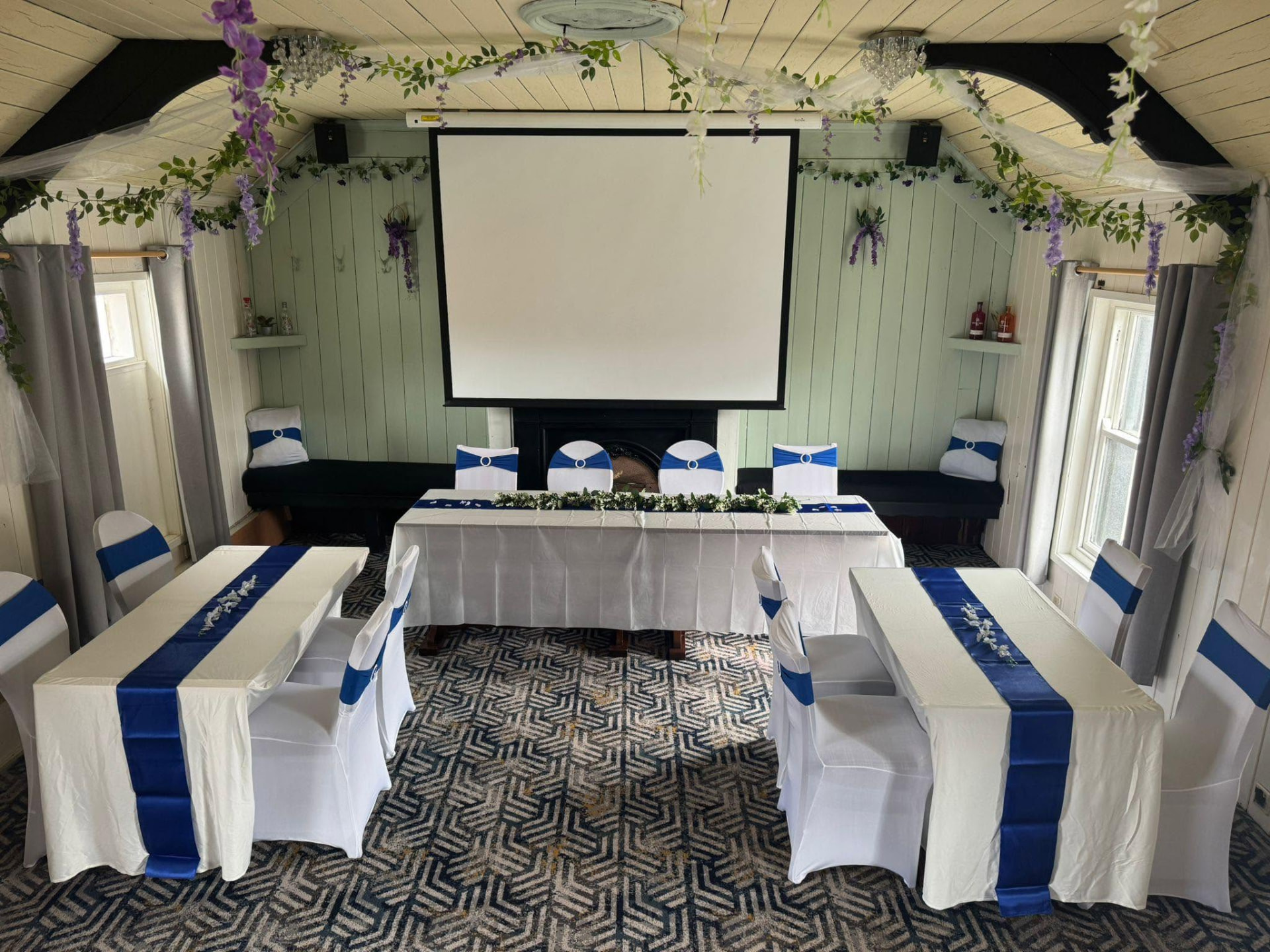 The function room at The Wellington Inn laid out with white linen, blue table runners and a projector screen